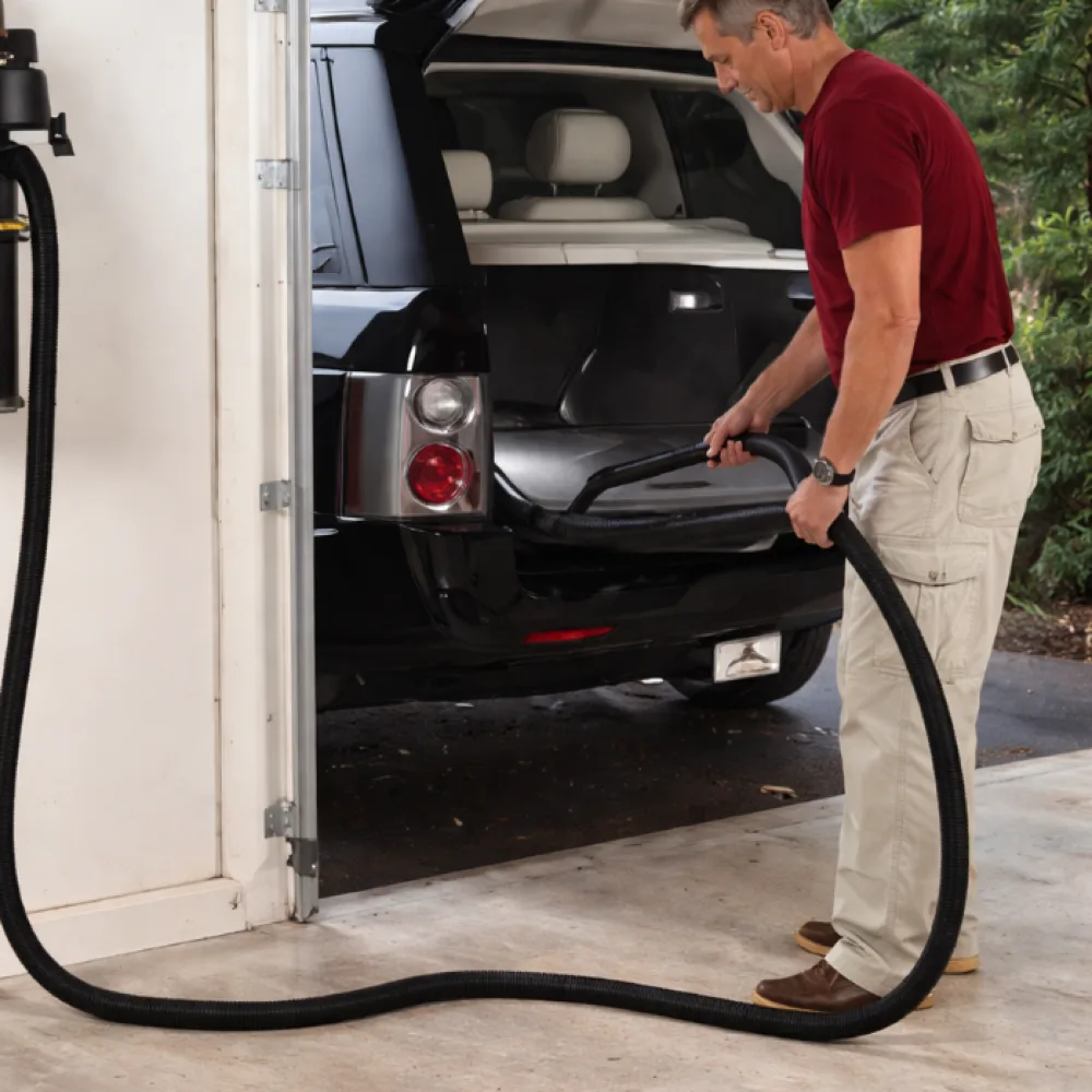 Man vacuuming a vehicle in the garage with a wall-mounted InterVac GarageVac